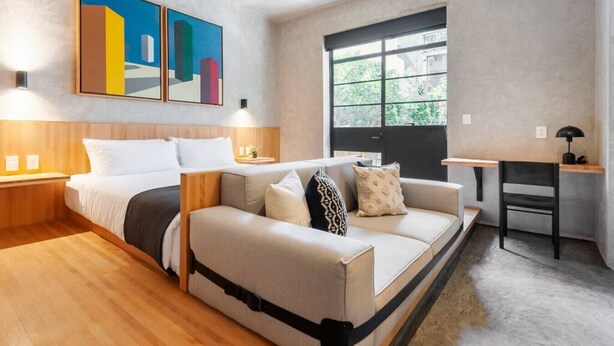 Une chambre d’hôtel moderne équipée d’un lit, d’un canapé, d’un bureau et d’une grande fenêtre.
