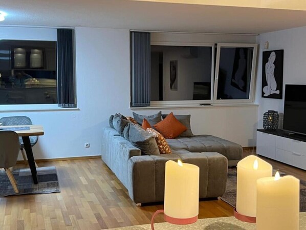 A modern living room with a grey sofa, two large candles, and a TV on a white cabinet.