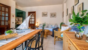 A room with a dining table, chairs, a sofa, a bed, and a large potted plant. - Sardinia RE - Flavia s Flat - Free Parking (Alghero)