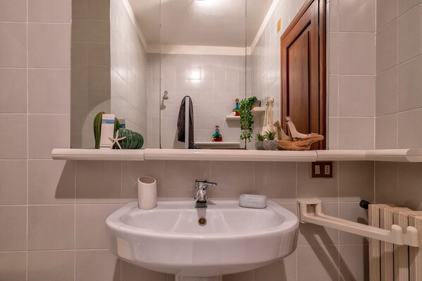 A bathroom with a white sink, a mirror, a towel rack, and a shelf with toiletries.