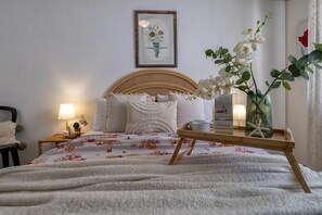 A neatly made bed with a floral bedspread, a bedside table with a lamp, and a tray with a cup and a book. - Sardinia RE - Flavia s Flat - Free Parking (Alghero)