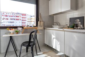 A modern kitchen with a dining area, a view of buildings, and a bag hanging on the wall.