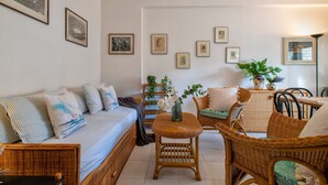 A room with a bed, a sofa, wicker furniture, and framed pictures on the wall. - Sardinia RE - Flavia s Flat - Free Parking (Alghero)