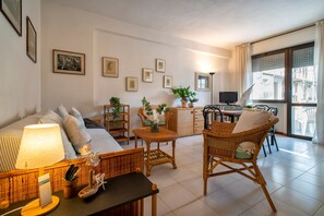 A living room with a sofa, a dining table, wicker furniture, and framed pictures on the wall. - Sardinia RE - Flavia s Flat - Free Parking (Alghero)