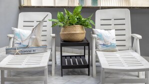 Two white lounge chairs with a woven basket and green plant between them, on a tiled floor.