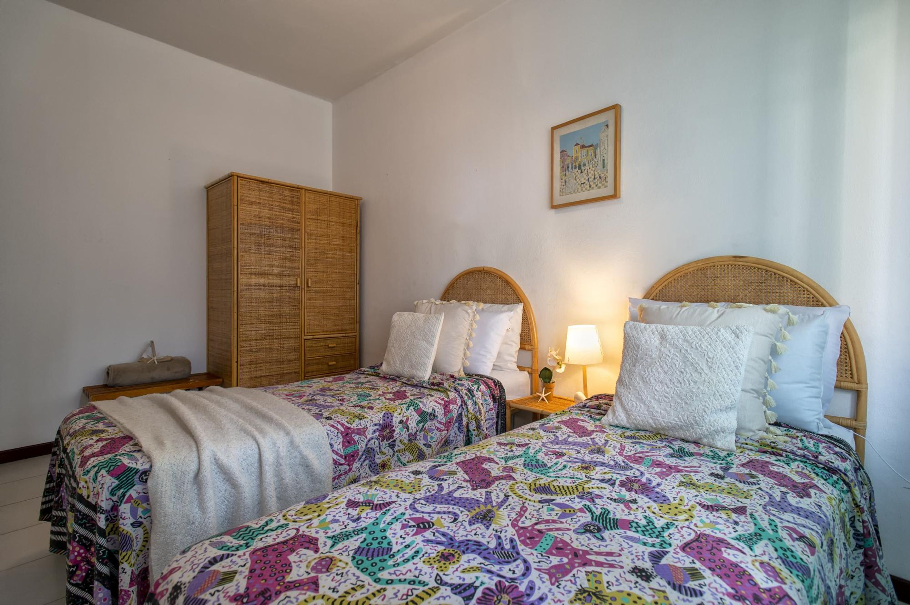 Une chambre avec deux lits, une armoire, une table de chevet avec une lampe et un tableau encadré au mur.