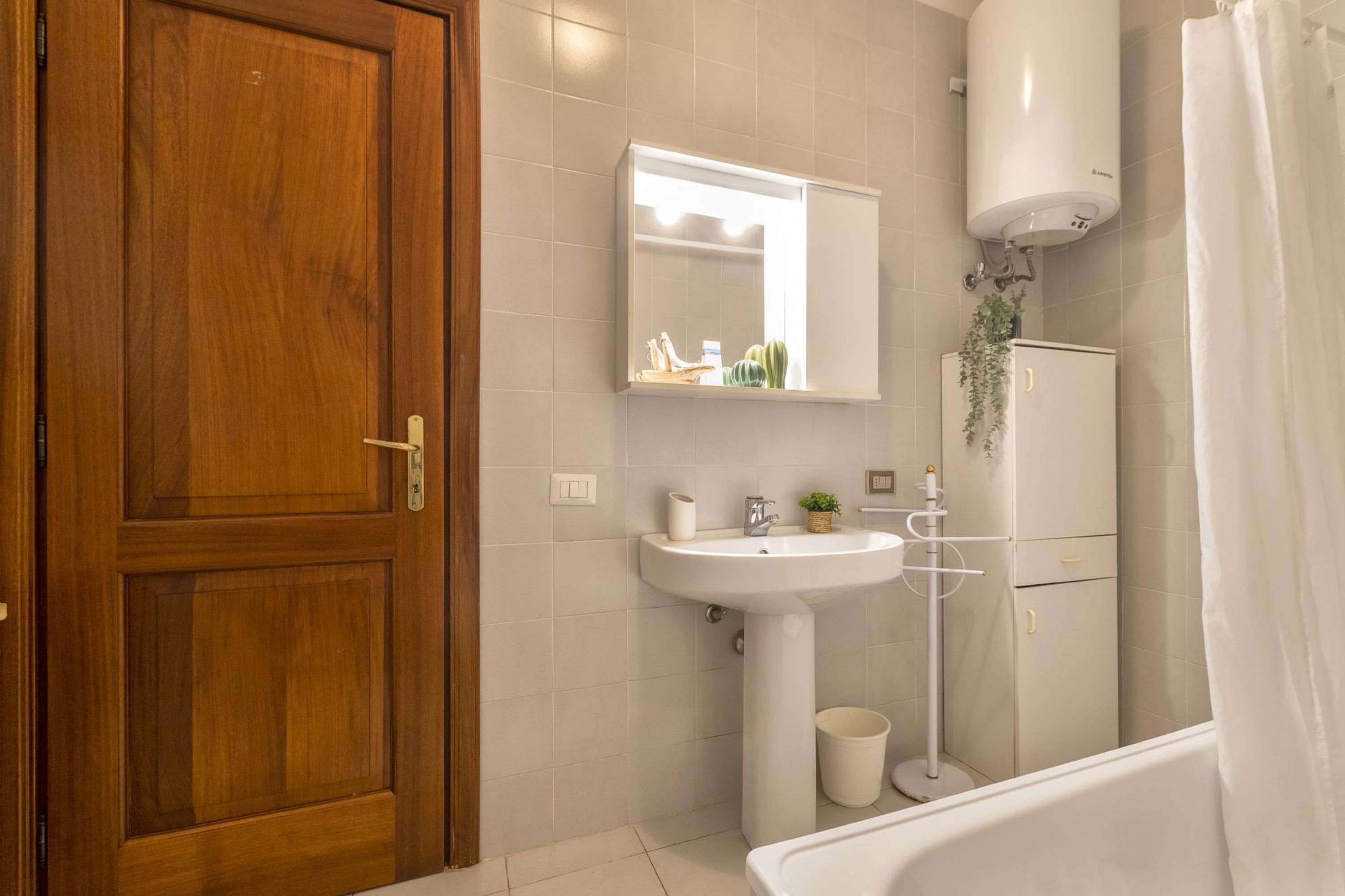 A bathroom with a wooden door, a white sink, a mirror, a toilet, and a shower curtain.