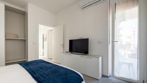 Une chambre moderne avec un lit, un téléviseur posé sur un meuble, une armoire et une porte-fenêtre coulissante donnant sur l’extérieur.