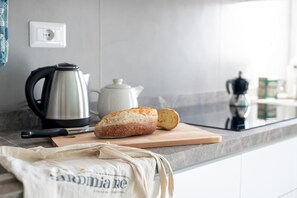 A kitchen counter with a loaf of bread, a cutting board, a kettle, and a coffee maker.
