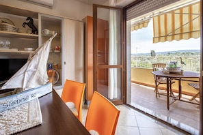 A room with a wooden table, orange chairs, a bookshelf, and a view of the outdoors through a sliding glass door.