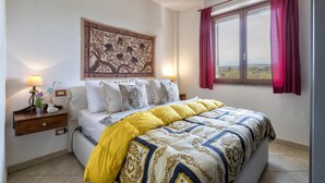Ein Schlafzimmer mit einem Bett, einem Nachttisch, einer Lampe, einem Fenster mit Vorhängen und einer Wanddekoration.
