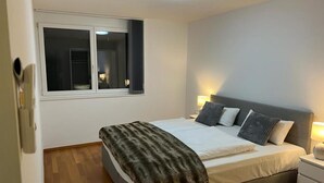 Ein Schlafzimmer mit einem Bett, Nachttischen, einem Fenster und einer Deckenleuchte.