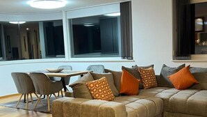 Ein modernes Wohnzimmer mit einem Ecksofa, einem Esstisch mit Stühlen und großen Fenstern.