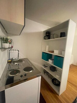 Une cuisine compacte équipée d’une cuisinière intégrée, d’un évier et d’une étagère avec des bacs de rangement.