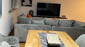 Ein modernes Wohnzimmer mit einem grauen Sofa, einem Holztisch und einem Flachbildfernseher.