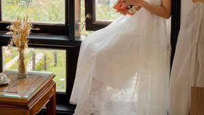 A room with a large window, a wooden table with a vase, and a white dress hanging by the window. - SeaColor Beachstay Danang Hotel Haviland (Da Nang)