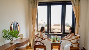 A room with two wooden chairs, a small table with a vase and a book, a mirror on the wall, and a potted plant. - SeaColor Beachstay Danang Hotel Haviland (Da Nang)