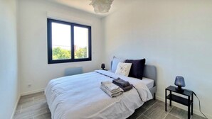 Ein Schlafzimmer mit Bett, Nachttisch, Lampe, Fenster und einer Pendelleuchte.