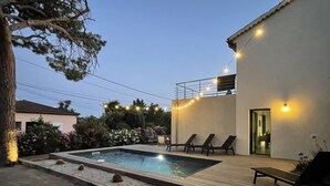 Ein Schwimmbecken mit Liegestühlen und Lichterketten, umgeben von einem Garten und einem Gebäude.