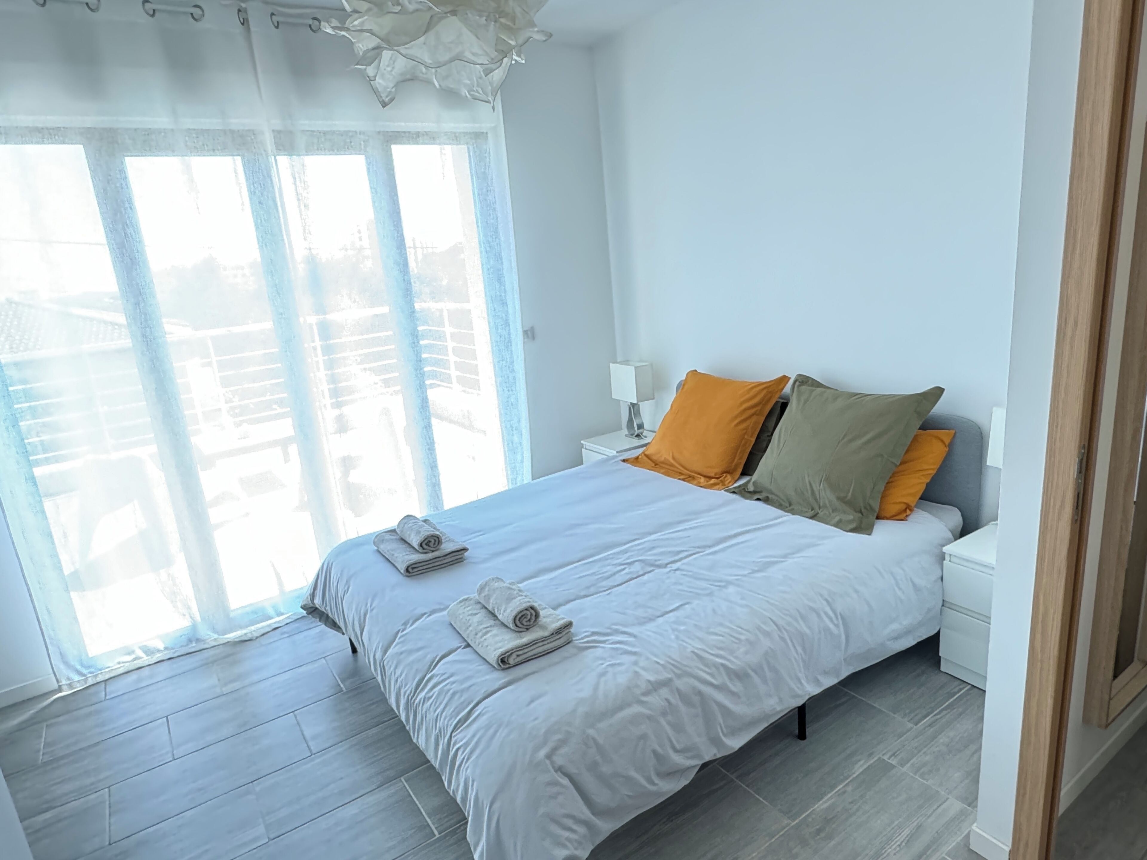 A modern bedroom with a large bed, two pillows, a nightstand, and a view through a glass door.