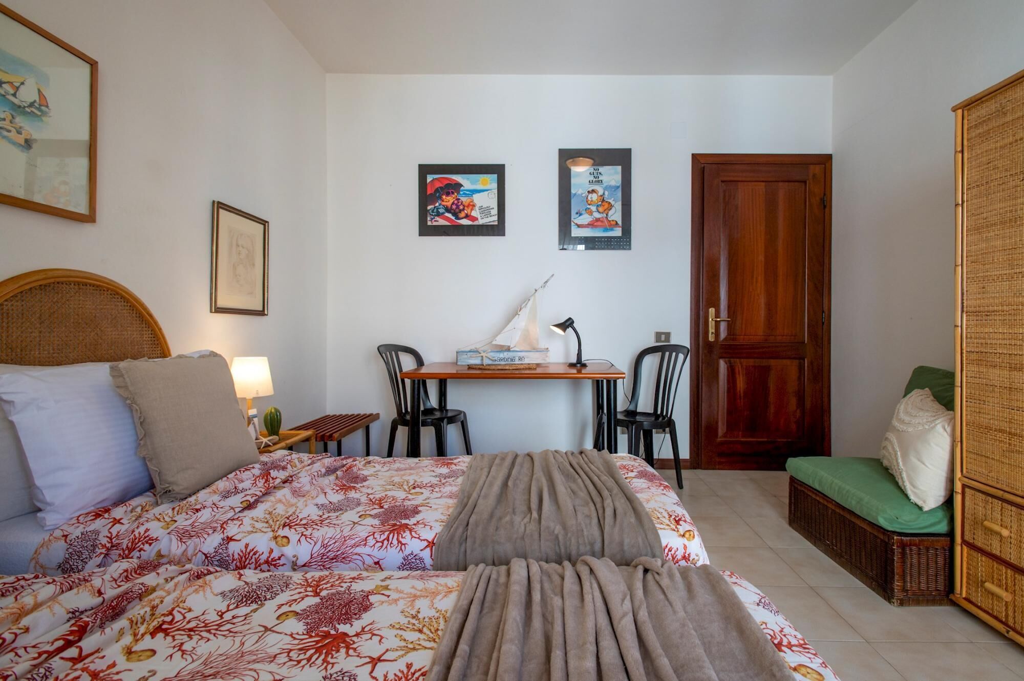 A bedroom with a bed, a desk with two chairs, a door, and a green chair.