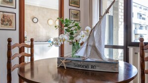 A round wooden table with a sailboat model, a vase with white flowers, and framed pictures on the wall. - Sardinia RE - Francesca s Flat - Free Parking (Alghero)