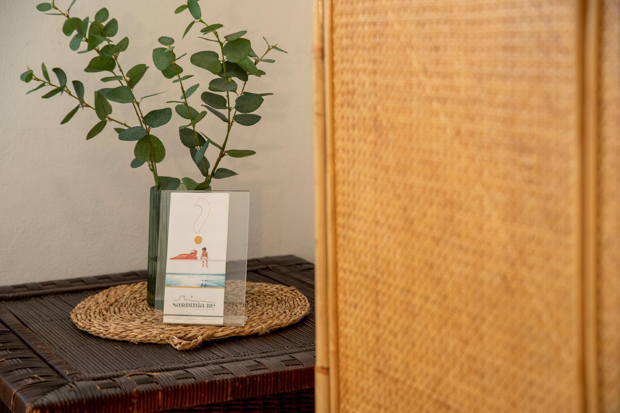 A clear glass vase with a book titled 'Sardinia Re' on a woven mat.