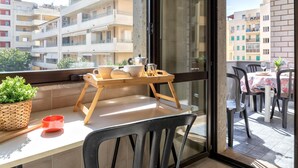 A balcony with a wooden table, chairs, a potted plant, and a table setting with a teapot and cups. - Sardinia RE - Francesca s Flat - Free Parking (Alghero)