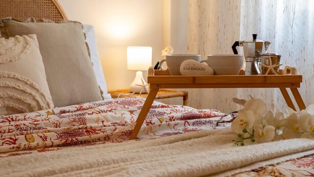 A neatly made bed with a patterned blanket, a wooden tray with a cup, bowl, and a starfish decoration, and a lamp on a bedside table. - Sardinia RE - Francesca s Flat - Free Parking (Alghero)