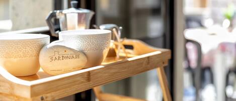 Una bandeja de madera con tres tazas de cerámica y una olla de metal sobre una mesa cerca de una ventana.