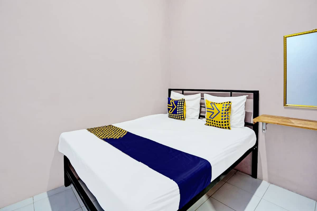 Een net opgemaakt bed met een wit-blauwe sprei, twee kussens met geometrische patronen, en een houten plank aan de muur.