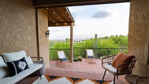 A covered patio with a white sofa, two wicker chairs, a small table, and a view of greenery and a cactus. - Hot Tub/Pool, Views, Pets-Catalina Foothills Casa (Tucson)