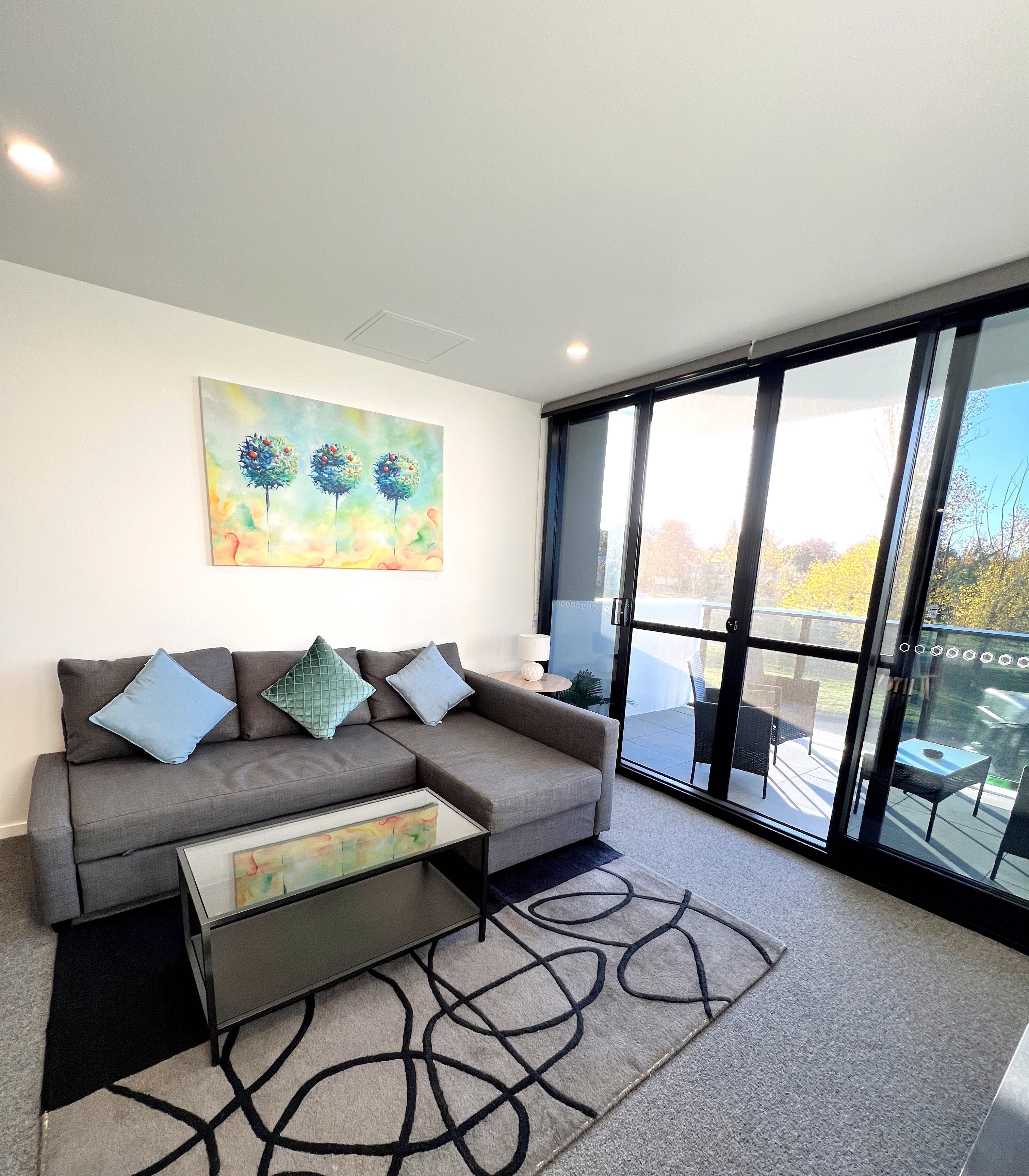 A modern living room with a grey sofa, a glass coffee table, and a colorful abstract painting on the wall.