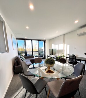 Uma sala de conferências moderna com uma mesa de vidro cercada por cadeiras, um sofá e uma TV.