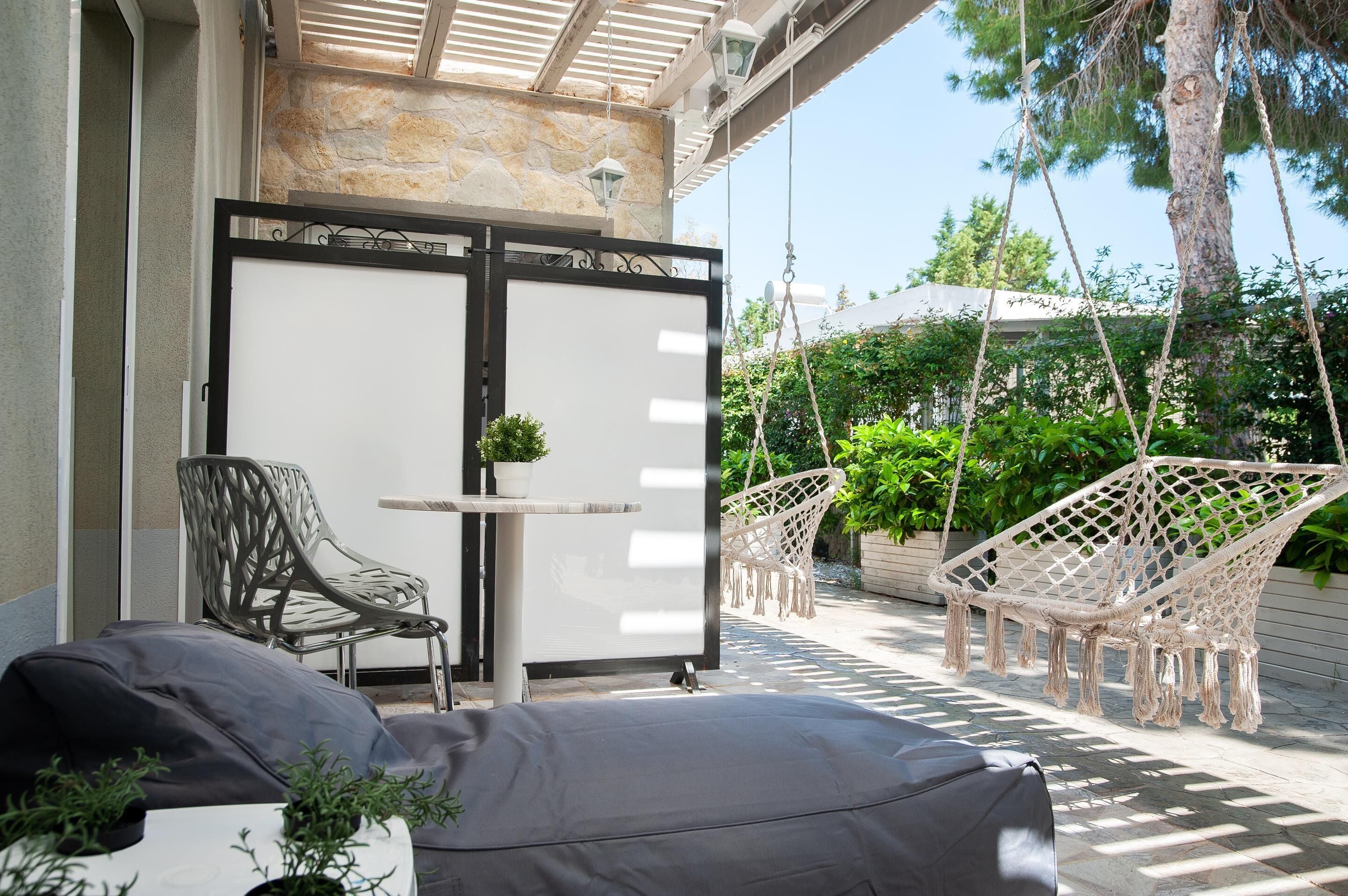 A covered patio area with a seating arrangement including a chair and a table, a swing chair, and a hammock.