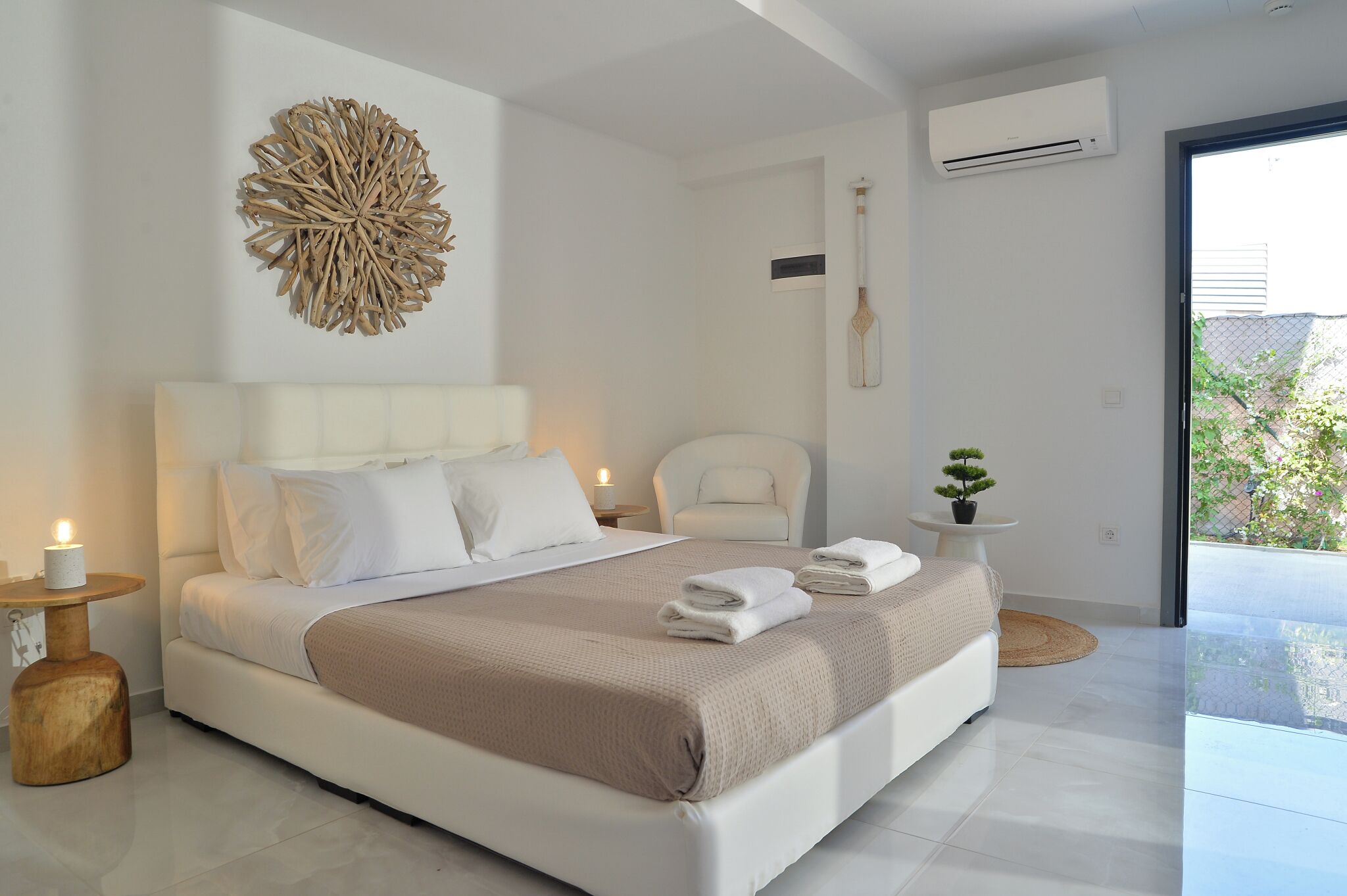 A modern bedroom with a large bed, a decorative wall piece, an air conditioning unit, a chair, and a small table with a plant.