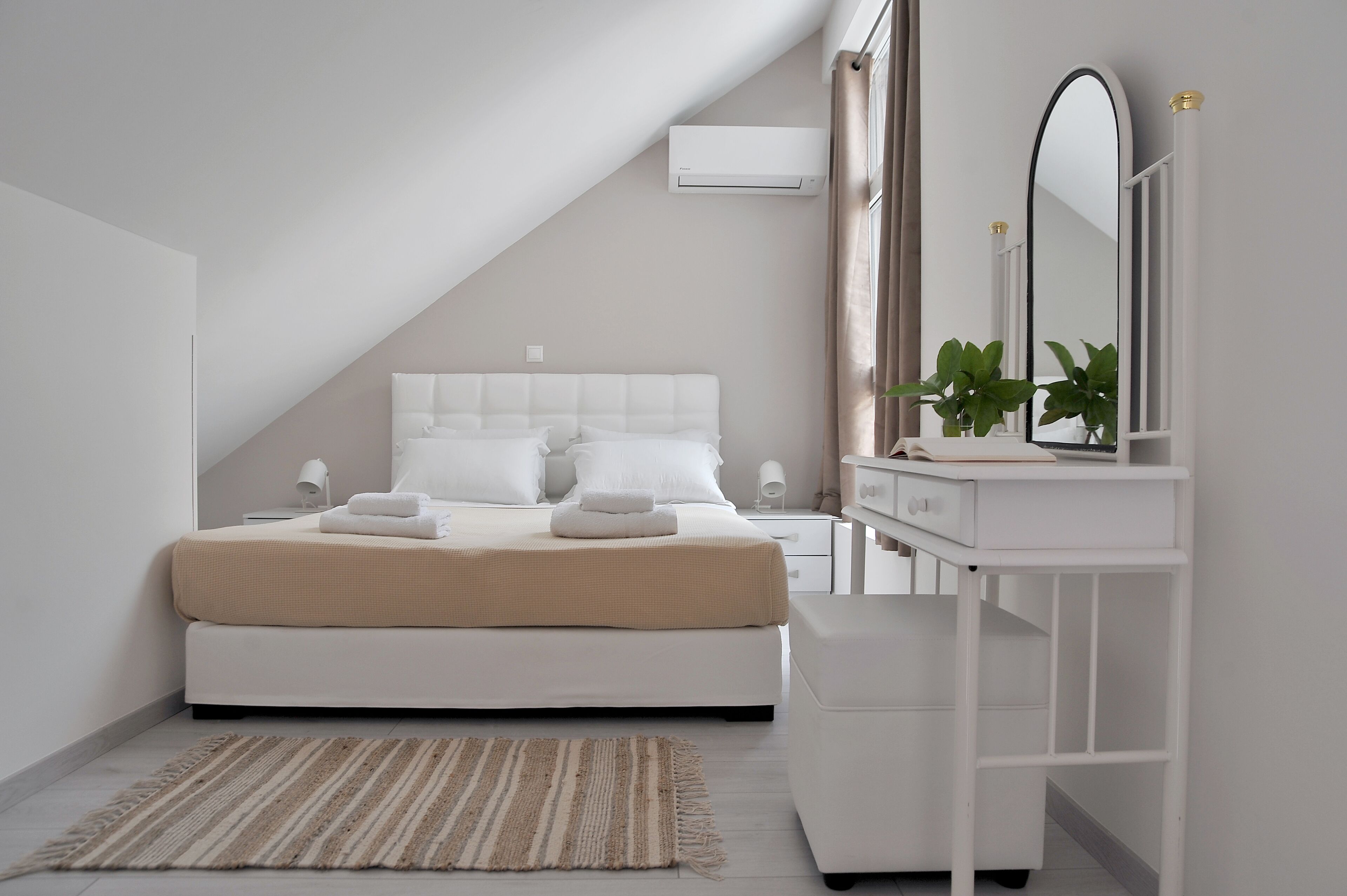 Um quarto moderno com uma cama branca, mesas de cabeceira, um espelho e uma pequena planta.