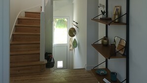 Un escalier mène à un palier d’où l’on peut admirer la verdure environnante. Une étagère fixée au mur, ornée de divers objets décoratifs, est visible.