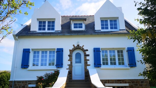 Une maison à deux étages, avec des fondations en pierre, des murs extérieurs blancs et des volets bleus.