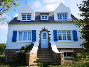 A two-story house with a stone foundation, white exterior walls, and blue shutters.
