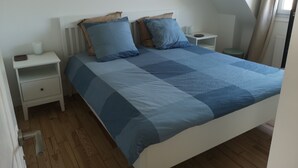 Une chambre à coucher avec un lit, deux tables de chevet, un plancher en bois et une fenêtre avec des rideaux.