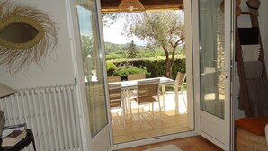 An open sliding glass door leading to an outdoor patio with a table and chairs, a woven basket, and a radiator inside. - Nyons ,villa au Cœur des Vignes et des Oliviers Avec Grande Piscine (Nyons)