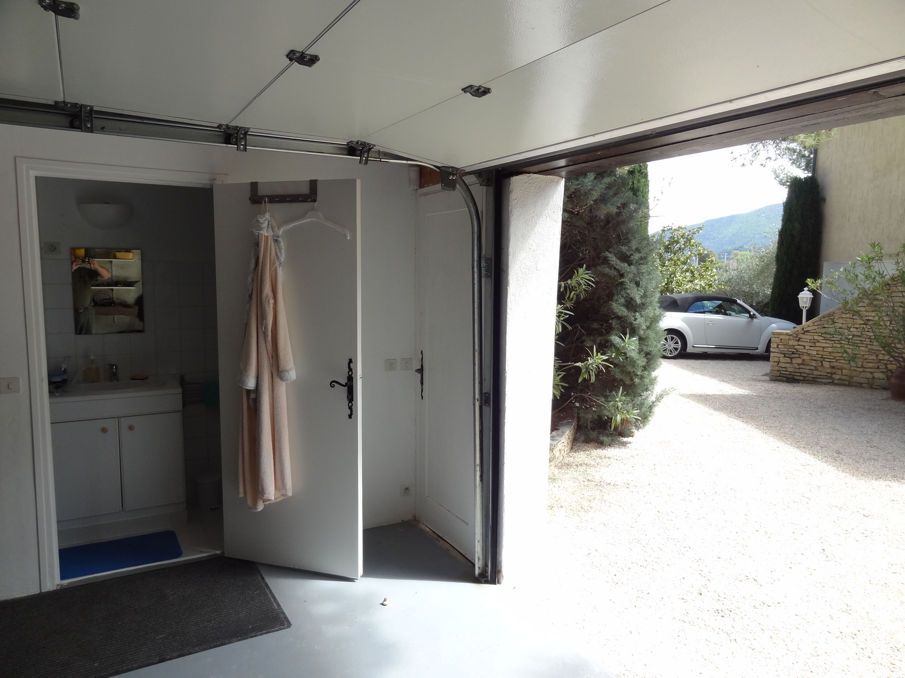 An open garage door leading to a driveway with a white car parked outside.