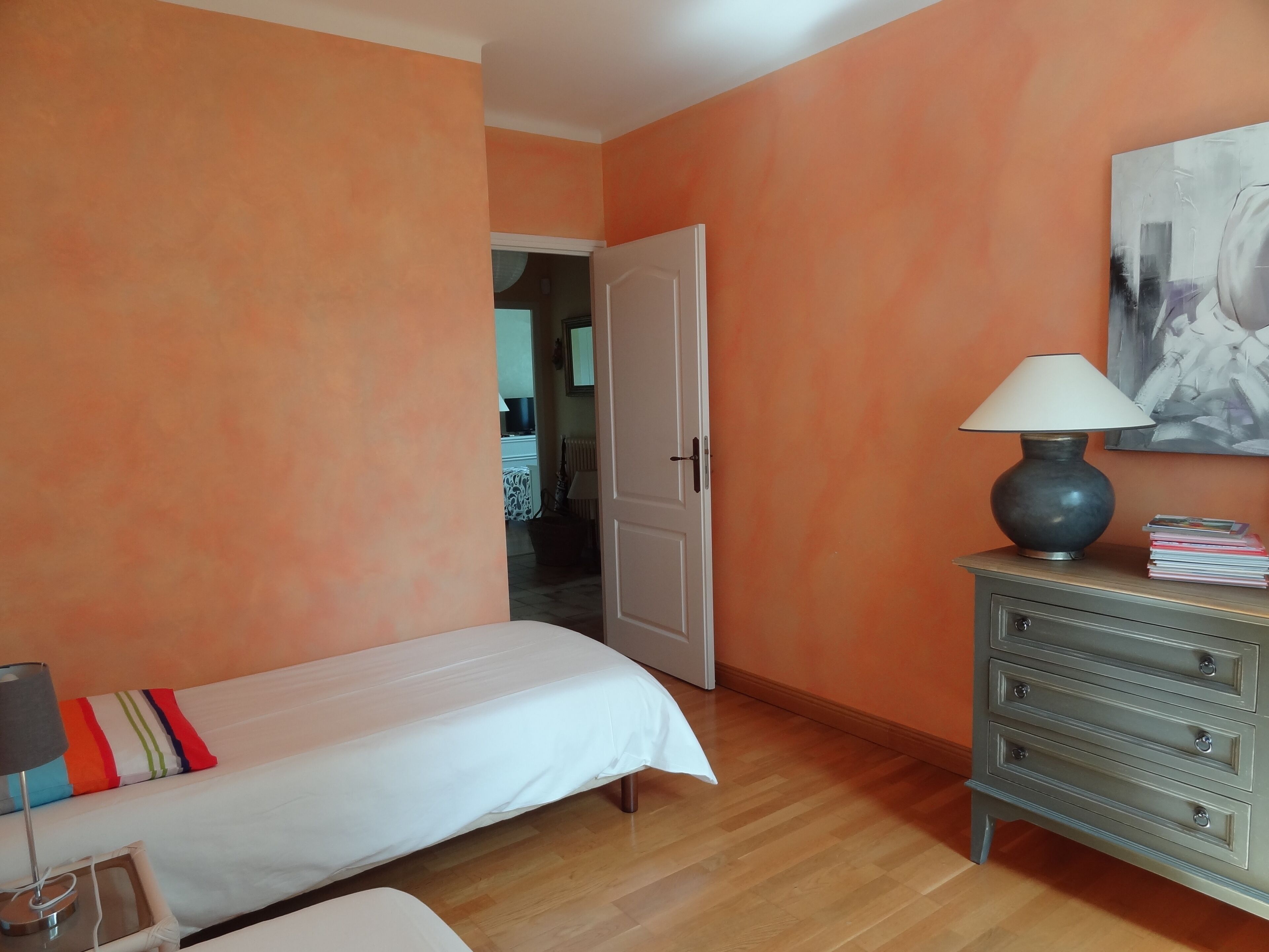 Un dormitorio con cama, cómoda, lámpara y un cuadro en la pared.