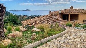 Ein Küstenhaus mit Ziegeldach, einem Steinweg und Blick auf das Meer und die entfernten Hügel.