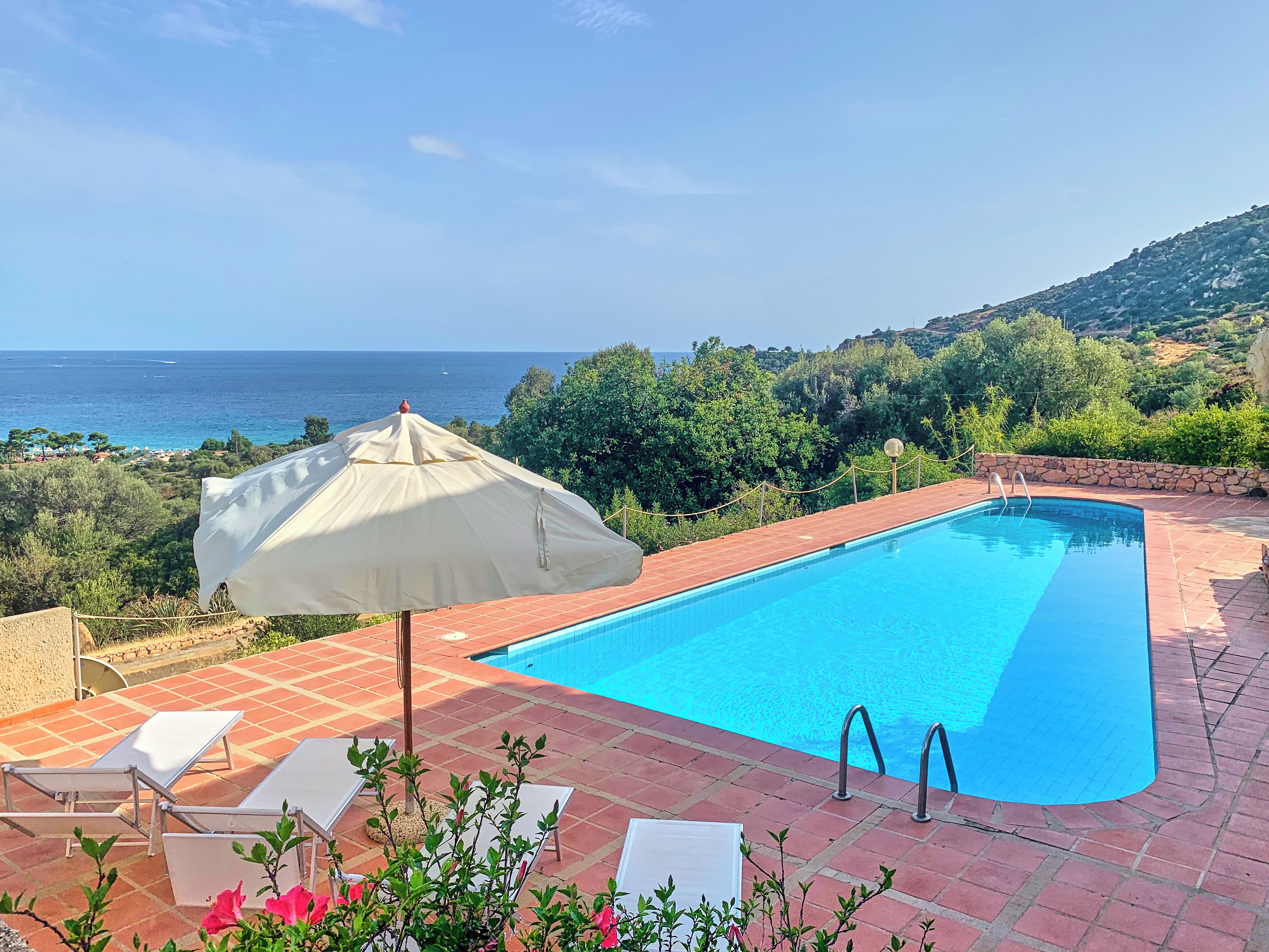 A rectangular swimming pool with a clear blue poolside area, a white umbrella, and lounge chairs.
