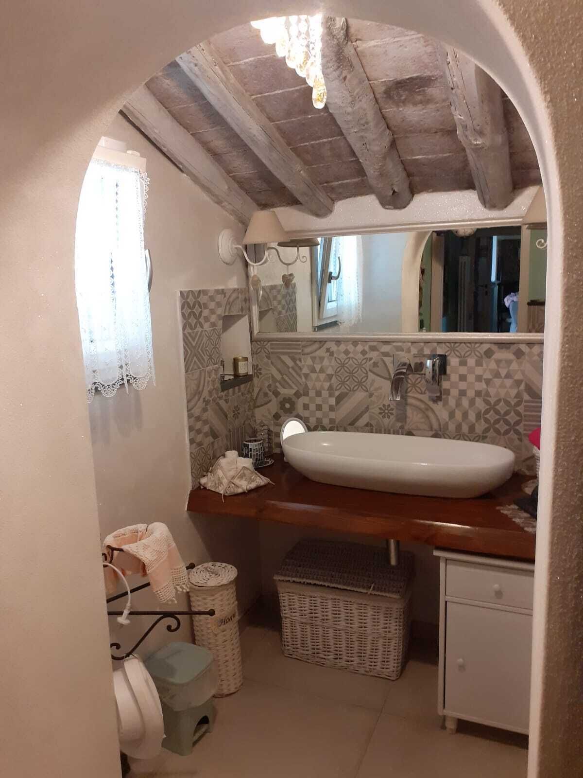 Un bagno con soffitto in legno, lavandino bianco, specchio e piastrelle decorate.