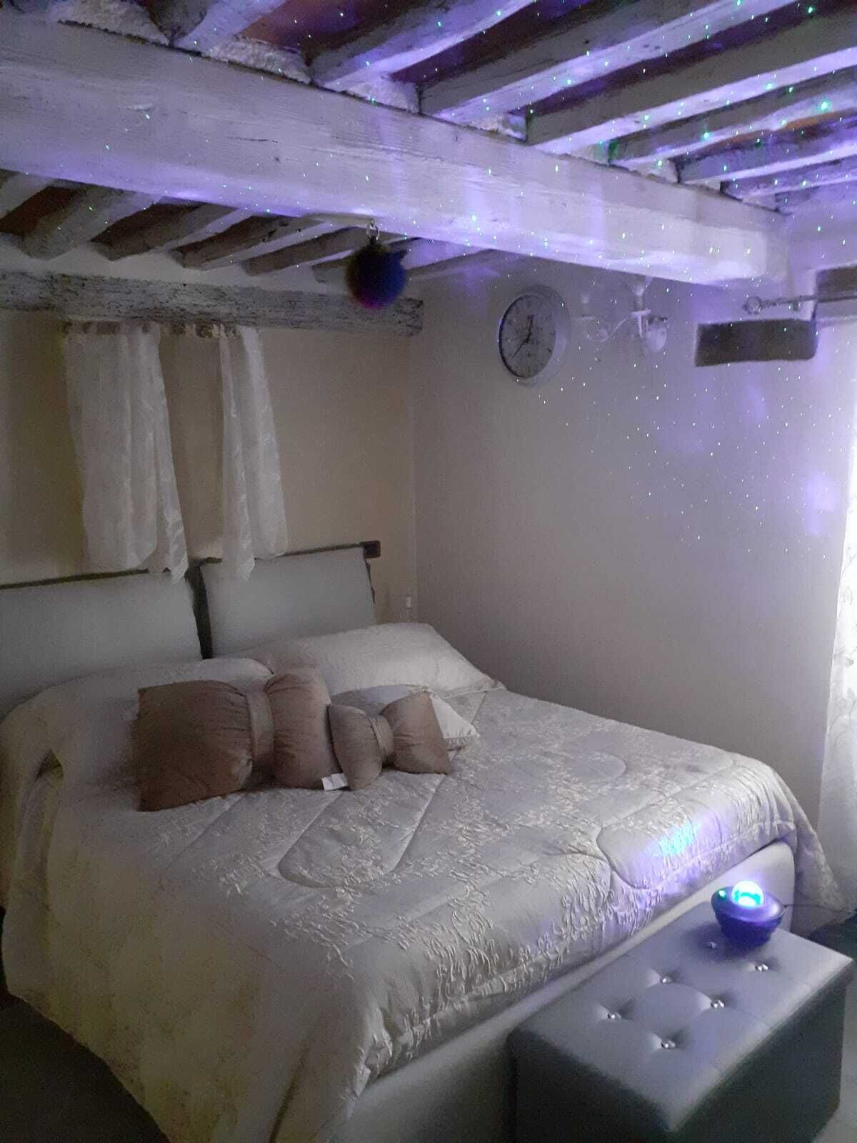 Ein Schlafzimmer mit einem Bett, Kissen, einem Nachttisch, einer Uhr und einer Decke mit freiliegenden Balken.