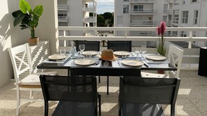 A table set for dining with white chairs, a potted plant, and a view of white buildings in the background. - Air-conditioned T3 apartment for 6 with terrace and parking in Port Leucate (Port Leucate)