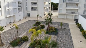 A modern multi-story residential building with balconies, a courtyard with palm trees, and a gravel pathway. - Air-conditioned T3 apartment for 6 with terrace and parking in Port Leucate (Port Leucate)